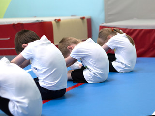 The boys is engaged in acrobatics. A childs dressed in a white t-shirt is doing exercises.