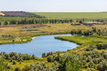 The summer landscape with a river among a farmland and farm buildings at the distance