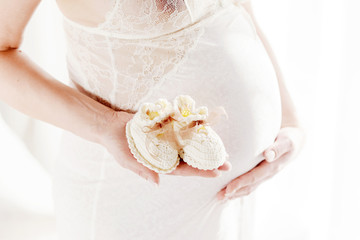 Close up on pregnant belly. Woman expecting a baby with a belly holding baby socks. Newborn baby booties in mothers hands.