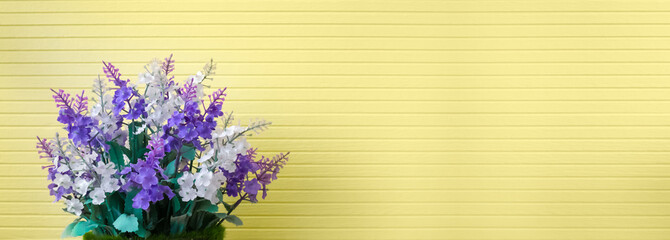 Beautiful purple lavender or lilac plastic flower bouquet in pretty vase on stripe textured yellow wallpaper background decoration in home spa for horizontal banner header on website