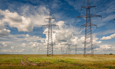 High voltage power lines in steppe covered with green and yellow grass under deep blue sky with heavy clouds at Khakassia, Siberia, Russia.