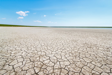 The view of the cracked soil on the salt lake coast with tiny stripe of the green grasses and water at the horizon. Gruzskoe lake, Rostov-on-Don region, Russia