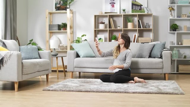 Young girl with a phone takes a selfie on the floor in a cozy living room