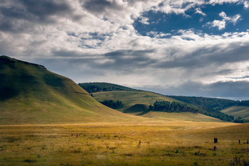 Grass hills covered with trees in steppe under spectacular clouds sky during sunset at Khakassia, Siberia, Russia.