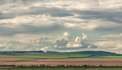 Agricultural fields on the hills in steppe unders heavy clouds sky at Khakassia, Siberia, Russia.