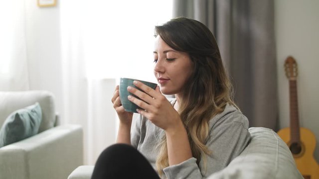 Young girl drinks tea from a large cup in the living room in the morning
