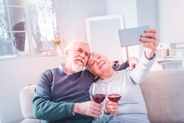 Elderly lady holding smartphone while making selfie with her husband