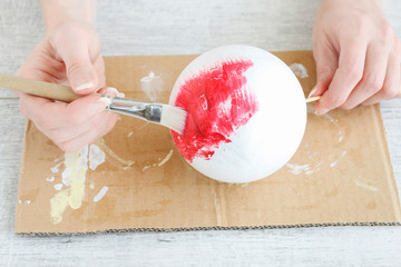 Woman paints on red color a styrofoam ball.
