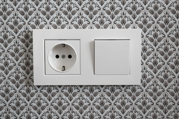 White plastic switched double socket. Light switch and power socket control panel on wall with wallpaper, close-up. Electrical european equipment