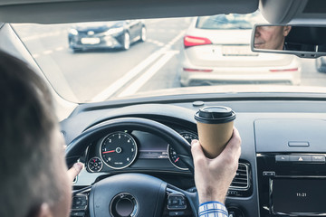 Elderly Businessman drinking coffee from paper cup while driving a car on the highway. Selective...