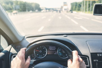 Selective focus of man hands on steering wheel driving a car on the speed highway. View from above