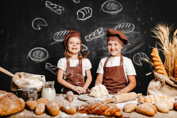 Adorable girl with brother in aprons on table with bread loaves making fresh dough and having fun