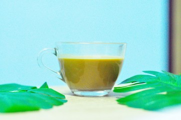 Latte coffee in a clear glass placed on a table with leaves on a blue background makes it refreshing in the morning.