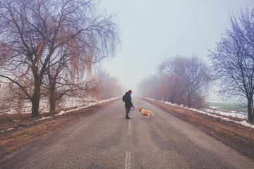 Man with Labrador retriever dog walking on the road in winter