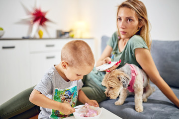 Single mom with TV remote, kid and dog in the living room.
