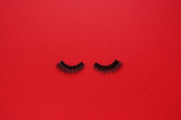 False eye lashes on red background with copy space, mockup. Beauty concept