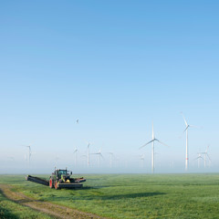 farmer mows grass near wind turbine farm in oastfriesland on misty summer morning