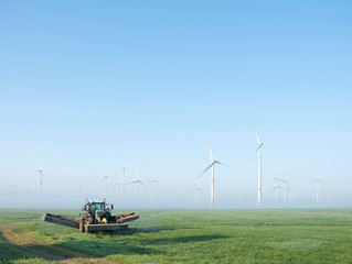 farmer mows grass near wind turbine farm in oastfriesland on misty summer morning © ahavelaar