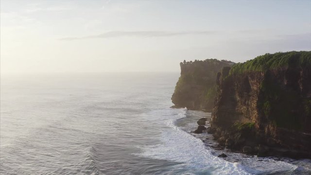 Aerial view of breathtaking cliffs above blue ocean. Silhouette of Uluwatu temple on the cliff top. Bali, Indonesia
