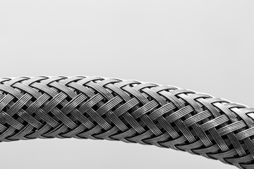 An extreme closeup view of a metallic hose, with criss cross silver strands woven, isolated against...
