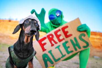 A message from the aliens in the rural scene. The alien holds a placard in his hands with the text and next to the dog