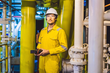 Young man in a yellow work uniform, glasses and helmet in industrial environment,oil Platform or...