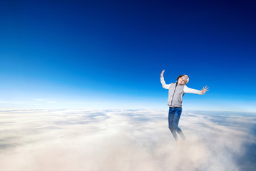 Fototapeta na wymiar Little girl flying over clouds in the blue sky.