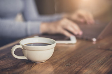 Young woman sitting in coffee shop at wooden table, drinking coffee and using laptop.