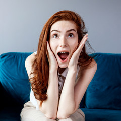 Redhead woman sitting on the blue couch at home.