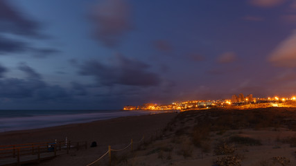 The skyline of La Mata, part of the Spanish city of Torrevieja, at the blue hour with beautiful clouds in the sky. The beach is deserted. The city is brightly lit.