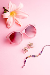 Glamorous woman accessories - watch, sunglasses, earrings. Feminine composition on pink background