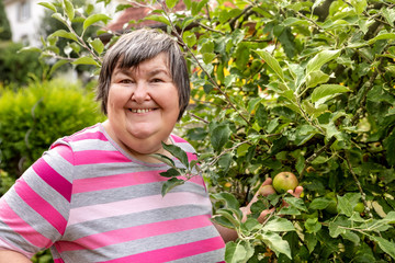 Geistig behinderte Frau steht an einem Apfelbaum, palliative Therapie durch Freude