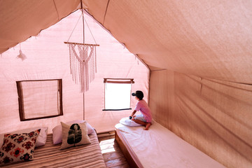 A cheerful little traveler is looking out the window of a canvas tent inside.