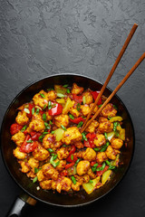 Gobi Manchurian in pan at black concrete background. Gobi Manchurian is Indian Chinese cuisine dish with cauliflower, tomatoes, onion, soy sauce. Copy space