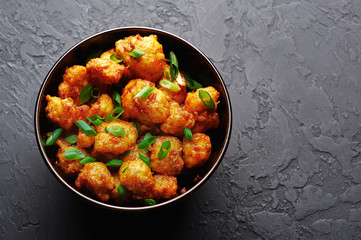 Gobi Manchurian in bowl at black concrete background. Gobi Manchurian is Indian Chinese cuisine dish with cauliflower, tomatoes, onion, soy sauce. Copy space