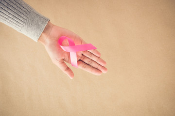 Woman hand giving satin pink ribbon, supporting symbol of breast cancer awareness campaign in October,