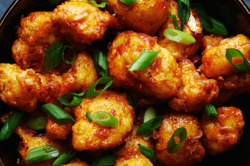 Gobi Manchurian in bowl at black concrete background. Gobi Manchurian is Indian Chinese cuisine dish with cauliflower, tomatoes, onion, soy sauce. Close up