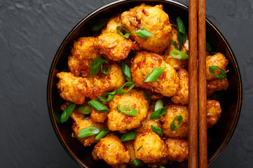 Gobi Manchurian in bowl at black concrete background. Gobi Manchurian is Indian Chinese cuisine dish with cauliflower, tomatoes, onion, soy sauce.