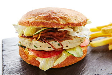 Fresh Chicken Burger with Onions, Tomato Sauce, Pickled Cucumbers, Green Lettuce, Turkey, Cheese and French Fries Garnish. Hamburger or Chickenburger on Natural Black Stone Plate Isolated on White