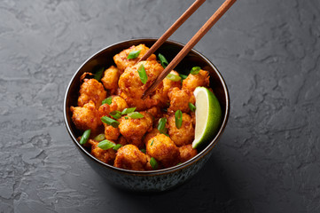 Gobi Manchurian in bowl at black concrete background. Gobi Manchurian is Indian Chinese cuisine dish with cauliflower, tomatoes, onion, soy sauce. Copy space