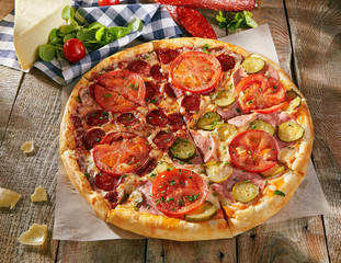 Pizza in half with salami, another - ham with pickled cucumbers and tomatoes sliced on wooden boards with vegetables