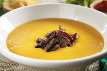White Bowl of Yellow Pumpkin Soup on Rustic Tablecloth Burlap Background