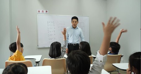 Asian teacher teaching children in the classroom at school. Little boy and girl raise hands together for accepting comments. Concept of education, experience learning and skill development.