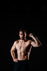 Fototapeta na wymiar Young bearded man with a kettlebell in his hands on a black background. bare-chested athlete