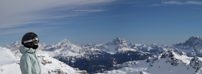A girl wearing helmet and ski goggles in front of unfocused Alpine mountains. Sas Pordoi. Dolomite Alps. South Tirol. Italy.