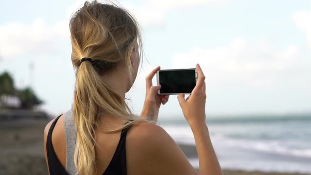 Young woman taking photo with cellphone on the beach