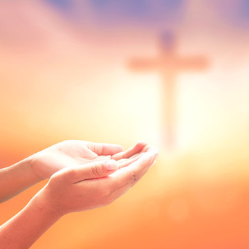 Human hands praying over blurred Christian cross on sunrise background