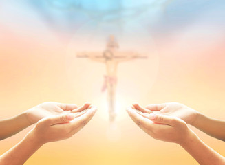 Hands of man praying over blurred crown of thorns and Jesus Christ on the cross over a colorful...