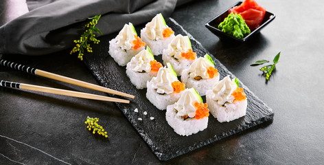 Roll with cream cheese cap, caviar and cucumber. Japanese cuisine restaurant menu item. Traditional asian appetizer, eastern cooking. Delicious sushi on wooden platter and chopsticks close up