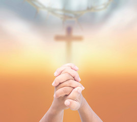 Human praying over blurred holy cross sunset background